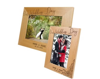 May include: Two wooden picture frames with the text "Our Wedding Day" engraved on them. The frames are both light brown and have a simple design. The top frame has a photo of a bride and groom in a forest setting. The bottom frame has a photo of a couple in a snowy setting. Both frames have the text "NAME & NAME" and a date engraved below the photos.