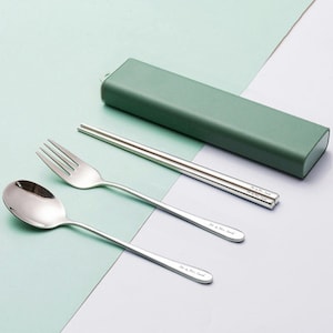 May include: A set of silver-toned cutlery in a green case. The set includes a fork, spoon, and chopsticks. The cutlery is engraved with the text "Mr. & Mrs. Smith".