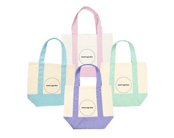 May include: Four canvas tote bags in pastel colors: light blue, pink, mint green, and lavender. Each bag has a cream-colored body with colored accents on the bottom and handles. A circular space for a logo is visible on each bag.