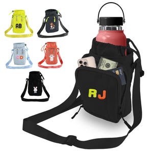 May include: A black water bottle carrier with a shoulder strap. The carrier has a zippered pocket on the front with the initials "RJ" embroidered in orange and yellow. The carrier has a separate pocket for a phone and a small pocket for cash or cards. The carrier is shown with a pink water bottle inside.