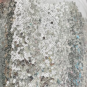 Puede incluir: Primer plano de una tela cubierta de peque&ntilde;as lentejuelas redondas plateadas. Las lentejuelas est&aacute;n densamente empaquetadas, creando un efecto brillante. Una tela blanca transparente es visible en la parte superior, agregando una capa de textura. El efecto general es glamuroso y llamativo.