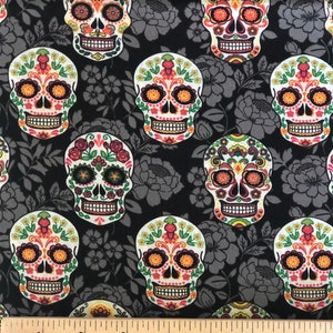 May include: Black fabric with a repeating pattern of colorful sugar skulls and gray floral designs. The skulls feature intricate floral and geometric patterns in orange, yellow, pink, and green. The fabric is measured in inches.