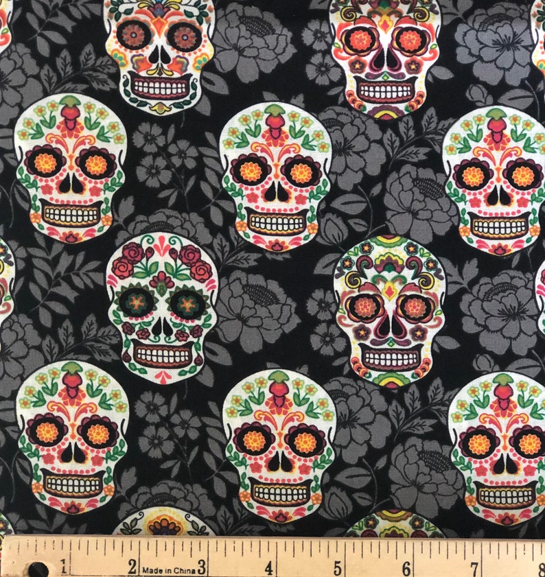 May include: Black fabric with a repeating pattern of colorful sugar skulls and gray floral designs. The skulls feature intricate floral and geometric patterns in orange, yellow, pink, and green. The fabric is measured in inches.