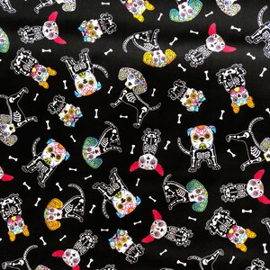 May include: Black fabric featuring a repeating pattern of dog skeletons decorated with colorful floral designs, reminiscent of D&iacute;a de Muertos celebrations. White bone illustrations are scattered across the background.