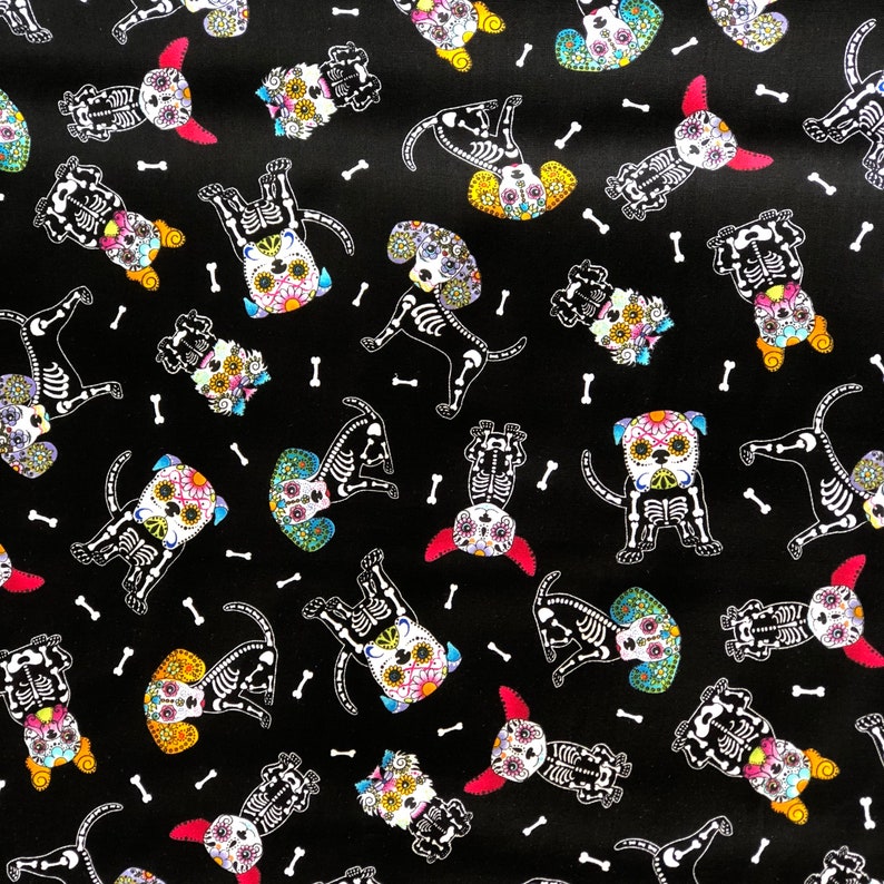 May include: Black fabric featuring a repeating pattern of dog skeletons decorated with colorful floral designs, reminiscent of D&iacute;a de Muertos celebrations. White bone illustrations are scattered across the background.