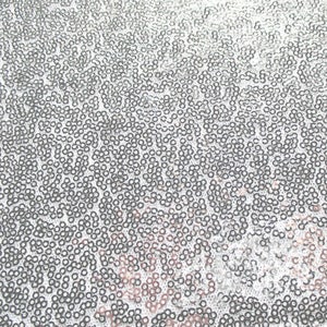 Puede incluir: Primer plano de una tela cubierta de peque&ntilde;as lentejuelas redondas plateadas. Las lentejuelas est&aacute;n densamente empaquetadas, creando una superficie brillante y texturizada. El efecto general es un material brillante y reflectante, adecuado para prendas de vestir o proyectos decorativos.