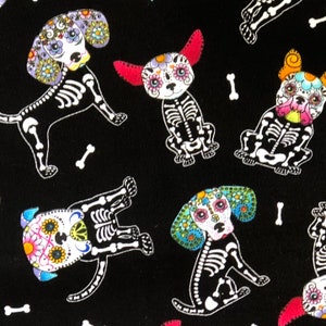 Pode incluir: Tecido preto com um padrão repetido de esqueletos de cães decorados com desenhos florais coloridos de caveiras de açúcar. Ossos brancos estão espalhados por todo o desenho. Os cães têm várias formas de orelhas e padrões florais.