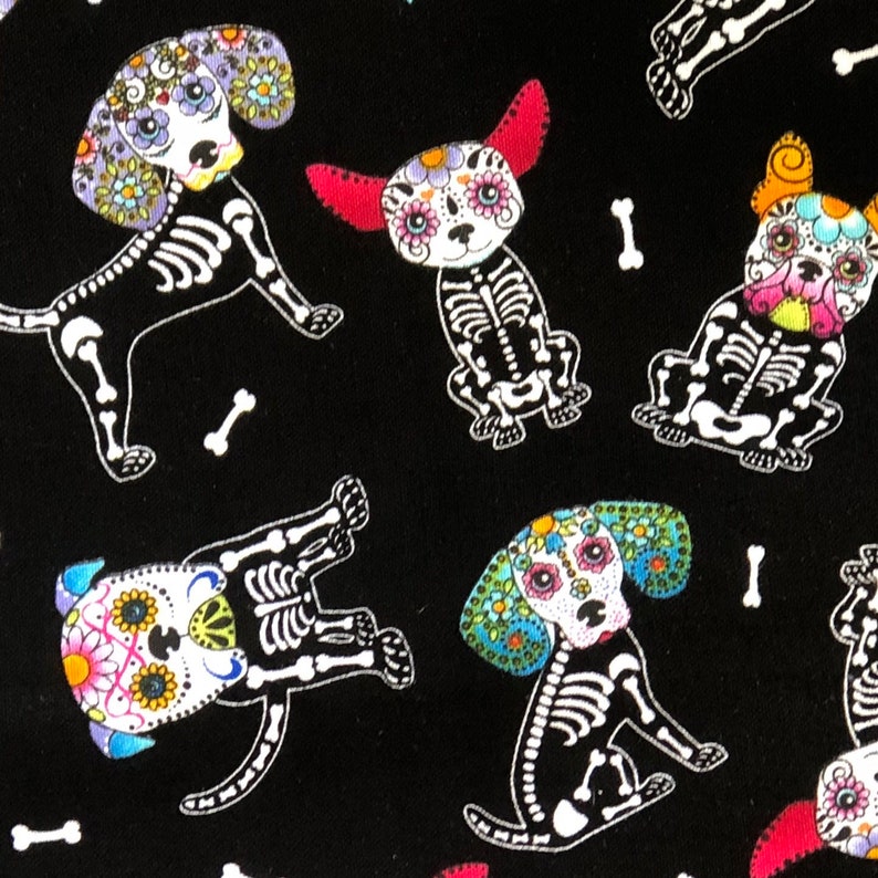 May include: Black fabric featuring a repeating pattern of dog skeletons decorated with colorful floral sugar skull designs. White bones are scattered throughout the design. The dogs have various ear shapes and floral patterns.