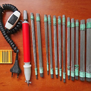May include: A red electric pen tool with a black cord and a white switch, along with a variety of metal tips bundled in green rubber bands. The tips are arranged in a row on a wooden surface.