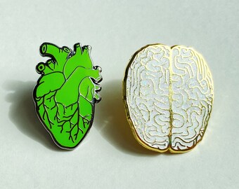 May include: Two enamel pins, one shaped like a green human heart and the other shaped like a white human brain.