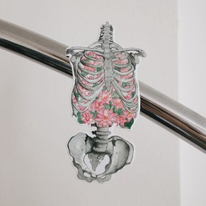 May include: A sticker of a human skeleton with pink and green flowers inside the rib cage.