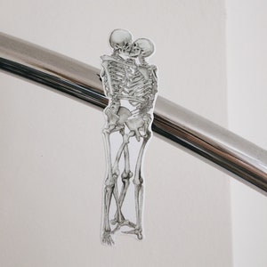 May include: Two skeletons are embracing and kissing. The skeletons are drawn in black and white and are attached to a silver railing.