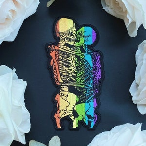 Op de afbeelding: Regenboog skeletpaar dat elkaar omhelst, een kleurrijk geborduurd patch.