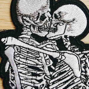 May include: Embroidered patch of two skeletons embracing, with white thread on a black background.