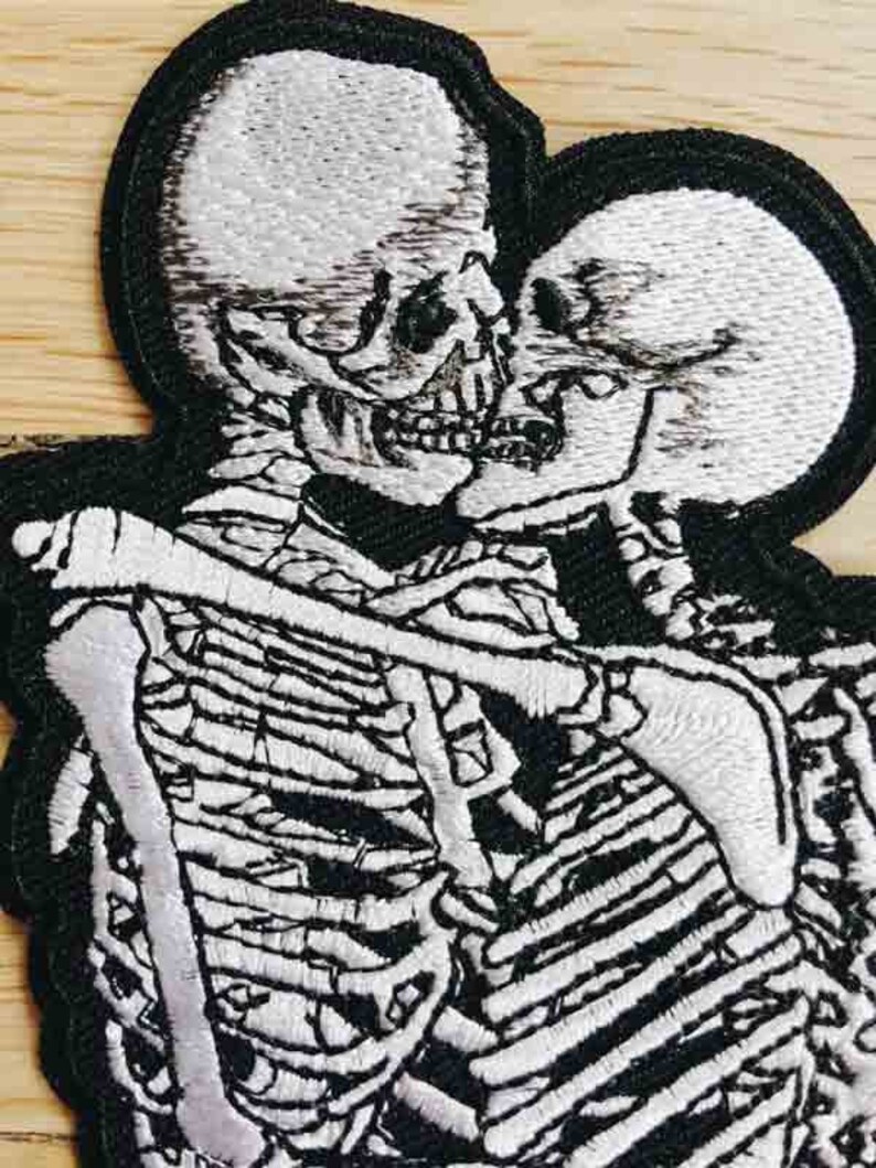 May include: Embroidered patch of two skeletons embracing, with white thread on a black background.