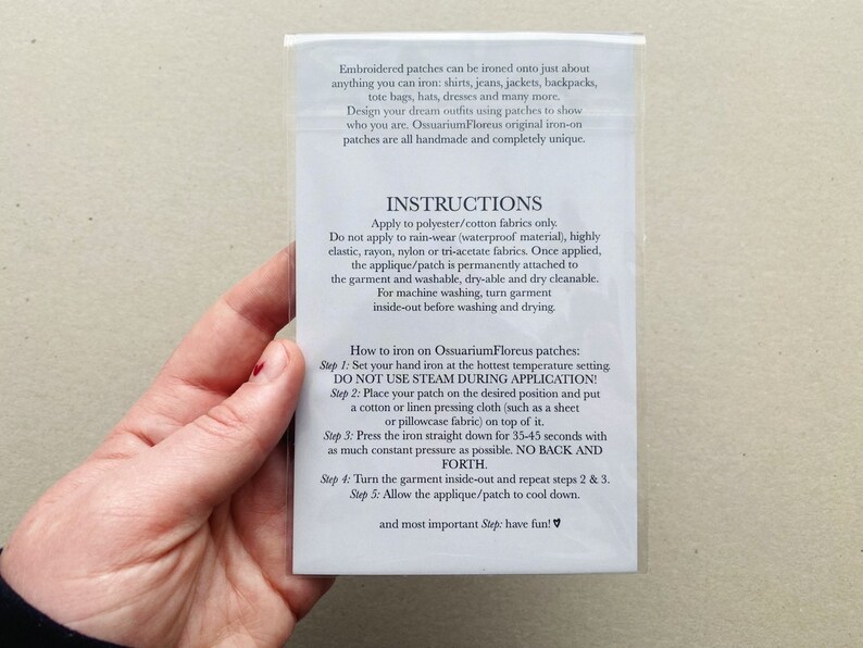 Puede incluir: Primer plano de una tarjeta blanca con instrucciones sobre c&oacute;mo planchar parches bordados. La tarjeta incluye el texto "Ossuarium Floreus" e instrucciones para aplicar los parches a la tela.