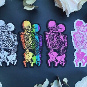 Puede incluir: Conjunto de cinco parches para planchar que representan esqueletos en un abrazo. Los parches son de varios colores, incluyendo blanco, arco&iacute;ris, rosa y negro.