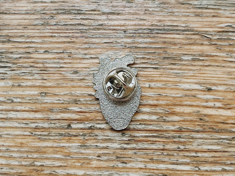May include: Silver-toned anatomical heart pin with a detailed design. The pin has a safety clasp on the back.