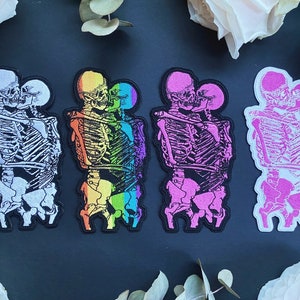 K&ouml;nnte beinhalten: Satz von f&uuml;nf B&uuml;gelbildern mit Skeletten in einer Umarmung. Die Patches sind in verschiedenen Farben, darunter Wei&szlig;, Regenbogen, Pink und Schwarz.