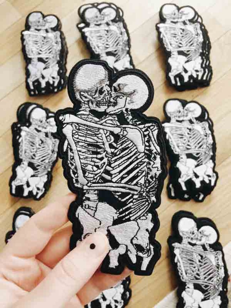 May include: A set of iron-on patches featuring a couple of skeletons embracing and kissing. The patches are black and white with a detailed design.
