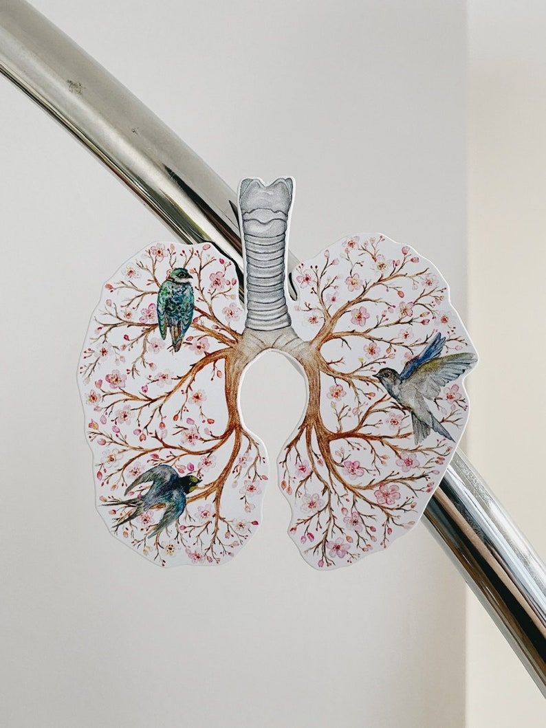 May include: A white paper cutout of a pair of lungs with a gray trachea. The lungs are decorated with pink cherry blossoms and three blue and green birds.
