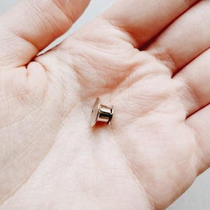 Op de afbeelding: Een zilveren metalen pin achterkant, gebruikt om een ​​pin of badge aan kleding te bevestigen.