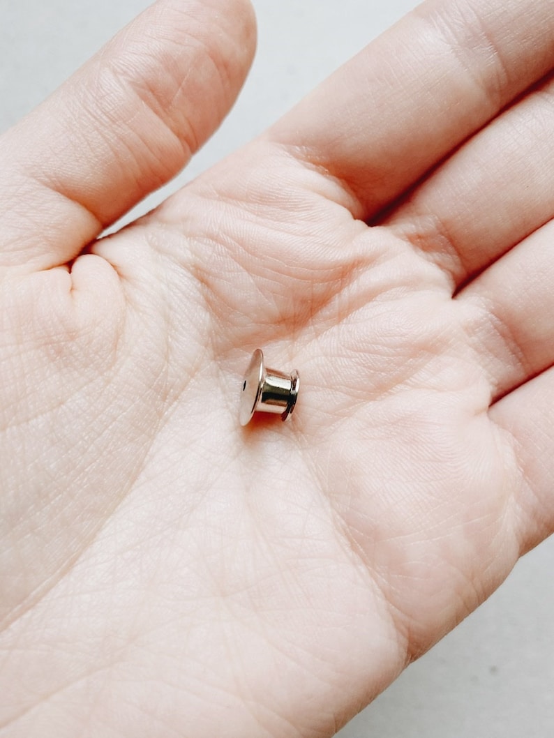 Op de afbeelding: Een zilveren metalen pin achterkant, gebruikt om een ​​pin of badge aan kleding te bevestigen.