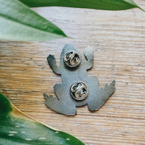 Op de afbeelding: De achterkant van een zilveren kikker broche met twee metalen sluitingen.