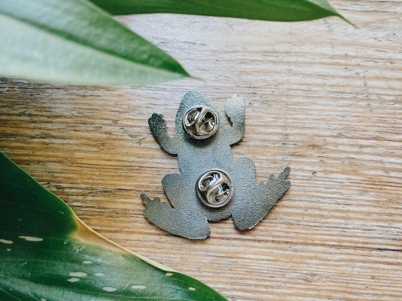 Op de afbeelding: De achterkant van een zilveren kikker broche met twee metalen sluitingen.