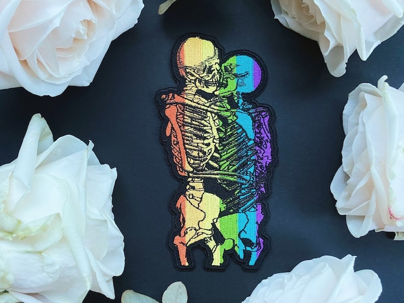 Puede incluir: Pareja de esqueletos arco&iacute;ris abraz&aacute;ndose, un parche bordado colorido.