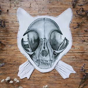 May include: A detailed black and white drawing of a cat skull with whiskers on a wooden surface.