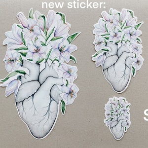 May include: Three sizes of a sticker featuring a white anatomical heart with white lilies growing from it. The sizes are labeled "L", "M", and "S".