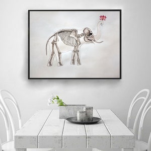 May include: A black framed print of a skeletal elephant with a pink lotus flower on its trunk. The print is hanging on a white wall above a white table with two white chairs.