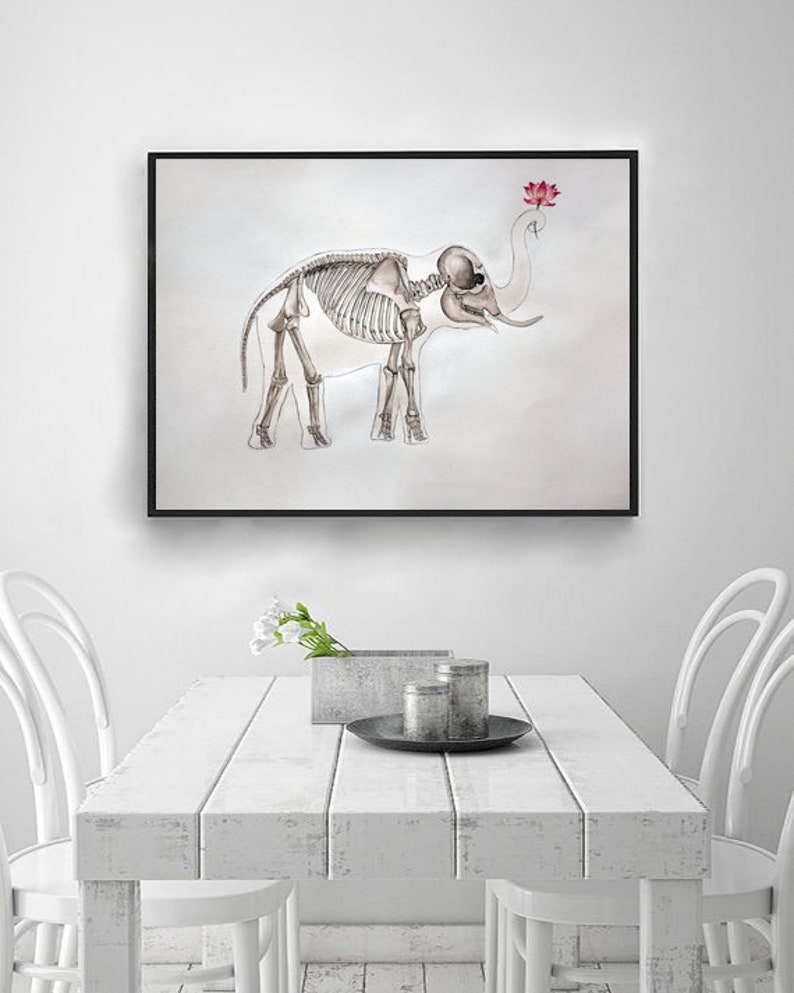 May include: A black framed print of a skeletal elephant with a pink lotus flower on its trunk. The print is hanging on a white wall above a white table with two white chairs.