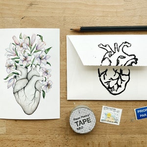 May include: A watercolor painting of a human heart with white lilies growing out of it. The heart is gray and the lilies are white with pink accents. The painting is on a white card.
