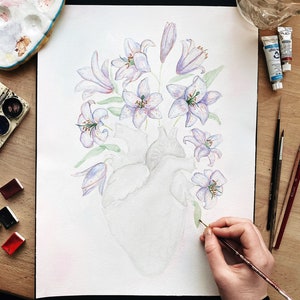 May include: A watercolor painting of a human heart with purple and white lilies growing from it. The artist is adding details to the painting with a paintbrush.