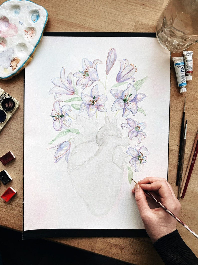 May include: A watercolor painting of a human heart with purple and white lilies growing from it. The artist is adding details to the painting with a paintbrush.