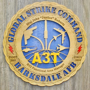May include: Wooden plaque with a layered design featuring the text "GLOBAL STRIKE COMMAND" and "BARKSDALE AFB". The plaque includes a blue center with aircraft silhouettes and the text "A3T". Dates "01OCT 2021" and "01NOV 2024" are also visible.