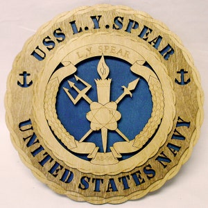 May include: A wooden plaque with a blue and brown design. The plaque features the text "USS L.Y. SPEAR UNITED STATES NAVY" and a crest with a torch, trident, and spear. The crest also includes the text "L.Y. SPEAR AS-30".