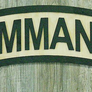 Puede incluir: Un letrero de madera con un borde negro y la palabra "COMMANDO" en letras negras sobre un fondo beige.