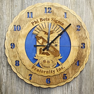 May include: Wooden wall clock with a layered design. The clock features a blue center with the Phi Beta Sigma Fraternity Inc. emblem and text. The numbers are in blue, and the clock hands are black.