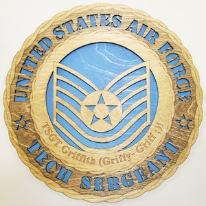 Pode incluir: Uma placa de madeira com um design azul e castanho. A placa apresenta as palavras "United States Air Force" e "Tech Sergeant". A placa também apresenta um design de chevron azul e castanho com uma estrela no centro. O texto "TSGT Griffith (Griffy-Griff)!"