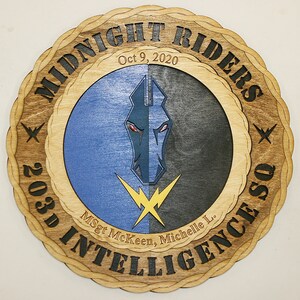 May include: A wooden plaque with a circular design featuring a black and blue horse head with a yellow lightning bolt. The text "MIDNIGHT RIDERS" is written in a circular pattern around the horse head. The text "203D INTELLIGENCE" is written in a circular pattern around the bottom of the plaque. The text "Oct 9, 2020" is written above the horse head. The text "MSgt McKeen, Michelle L." is written below the horse head.