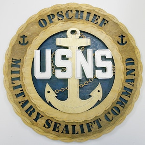 May include: A wooden plaque with a navy blue background and a gold anchor. The plaque reads "USNS Military Sealift Command Opschief".