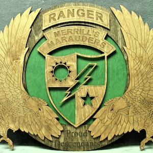 May include: A wooden plaque with a green background and a shield with a sun, lightning bolt, and star. The shield is surrounded by two eagle wings. The text "RANGER MERRILL'S MARAUDERS" is above the shield and "Proud Descendants" is below the shield.
