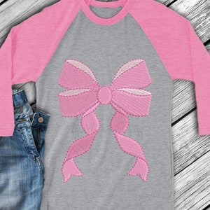 May include: A pink and grey long-sleeved shirt with a large pink embroidered bow on the front.