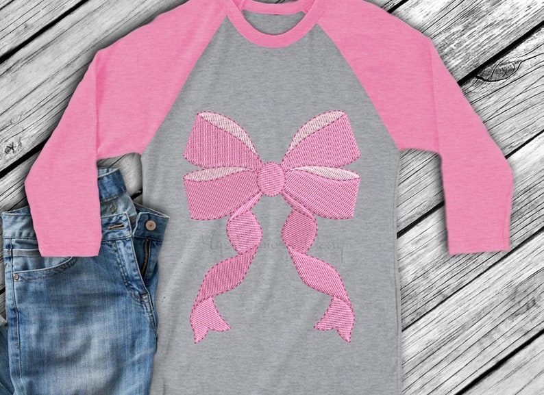 May include: A pink and grey long-sleeved shirt with a large pink embroidered bow on the front.