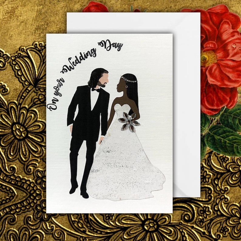 An interracial wedding card with a white groom and a black bride. The groom is wearing a black tuxedo and the bride is wearing a white a-line dress. the groom has shoulder length hair and the bride has long straight hair. The text on the card reads 'On your Wedding Day'.