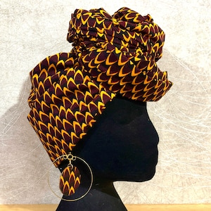 May include: A black head wrap with a yellow and brown geometric pattern. The wrap is tied in a turban style and has a large gold hoop earring.