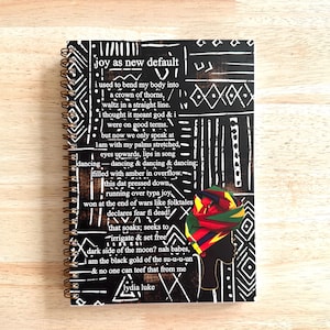 May include: A black and white spiral bound notebook with a colorful African print design and a quote that reads "joy as new default" by Lydia Luke.